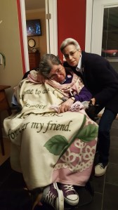 Two women, one in a wheelchair covered with a blanket, her shoes visible, and the other lean