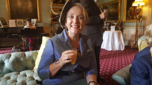 A woman smiling sitting with a drink in her hand in a living room with a red carpet
