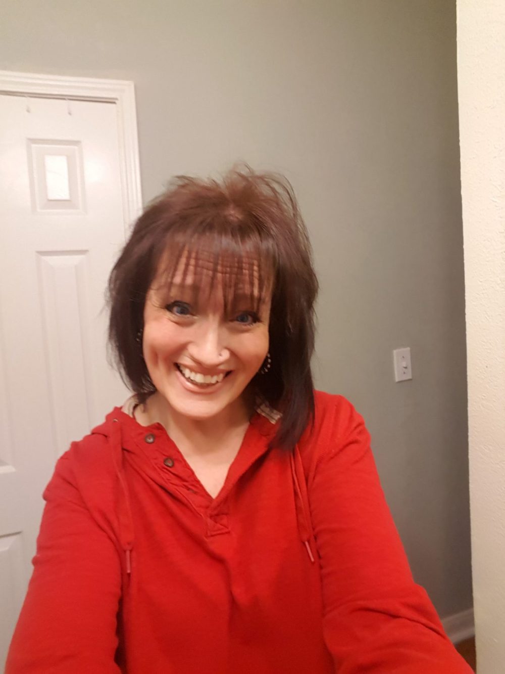 A woman with medium length brown hair, wearing a red long sleeve shirt with a hood