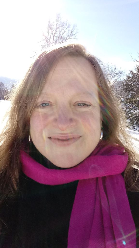 Headshot of Beth standing outside on a sunny, snowy day. She's wearing a magenta scarf and smiling while looking at the camera.