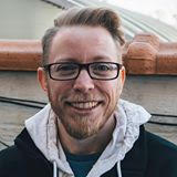 Headshot of a young man with glasses and facial hair smiling at the camera.