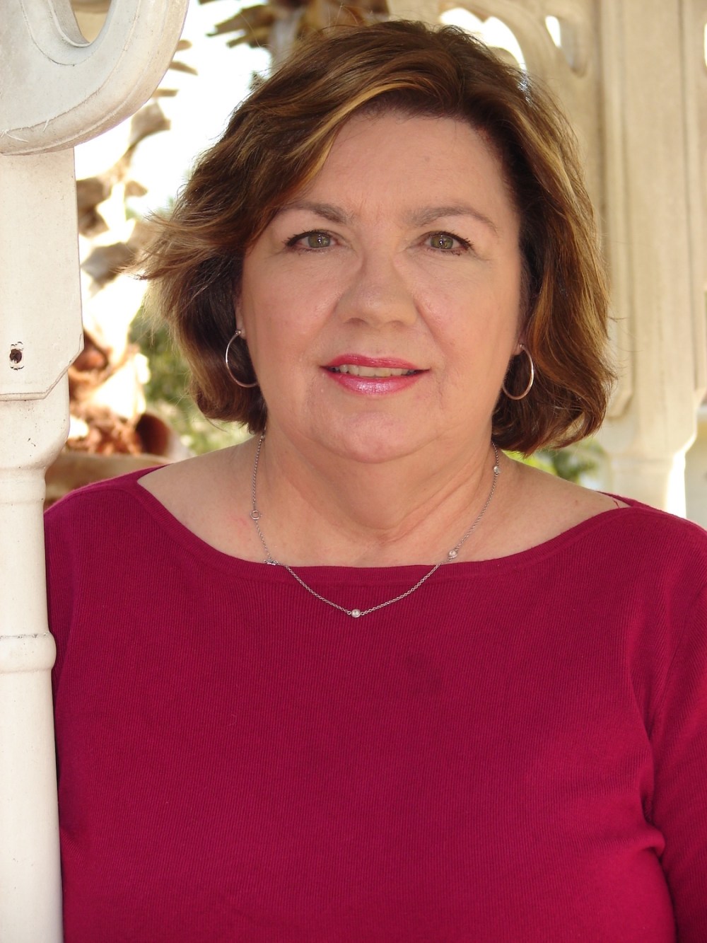 Headshot of middle aged woman with chin length brown hair wearing magenta sweater posed outdoors.