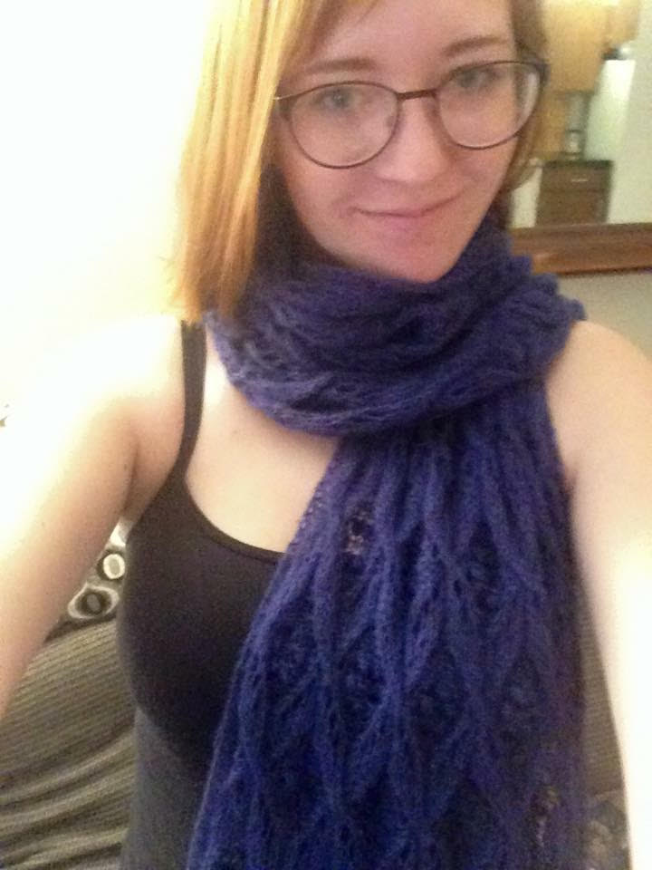 A smiling young woman with blonde hair wearing glasses, a black shirt, and a blue lace scarf.