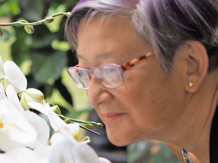 Closeup photograph of a woman with glasses bending down to smell white flowers.