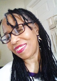 Akua,  an African Caribbean American Woman with braids and glasses, smiling