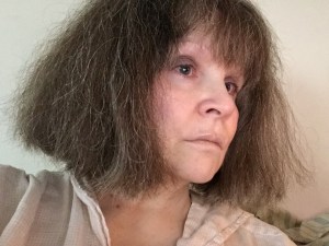 Photo of a woman's face, looking off to the right, with an open-collared white shirt, a serious expression, bob-length hair with bangs and small streaks of gray