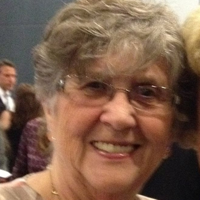 Woman with short grey hair and glasses smiles at the camera. 