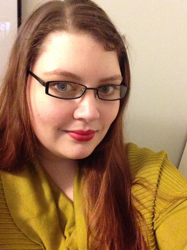 A woman with a mustard jumper, long brown hair and glasses. 