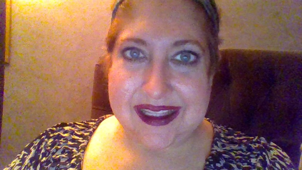 Me smiling, wearing dark pink lipstick, short hair pulled back, wearing a black and white shirt.