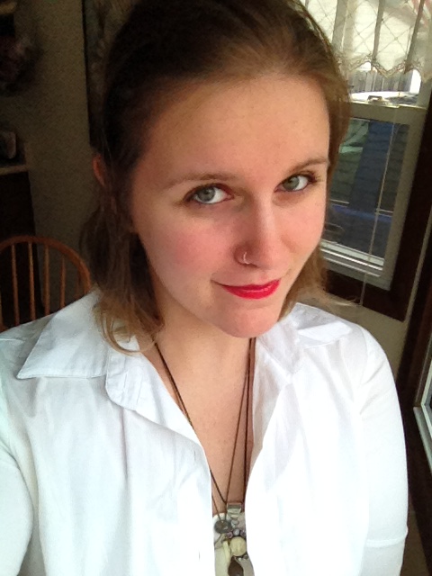 An effeminately presenting human being with bright red lipstick, short hair, a nose ring and a mischievous smile. 