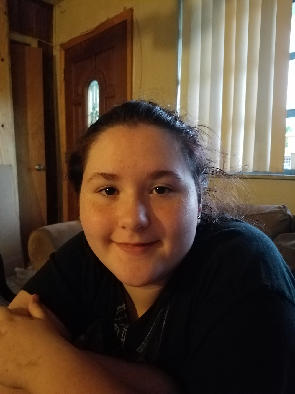 Headshot of a young woman sitting indoors, wearing a black shirt and smiling at the camera.