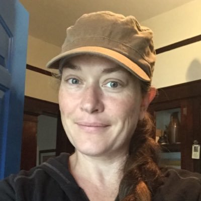 Headshot of Melissa indoors with a beige baseball cap on. She's smiling and looking directly at the camera.