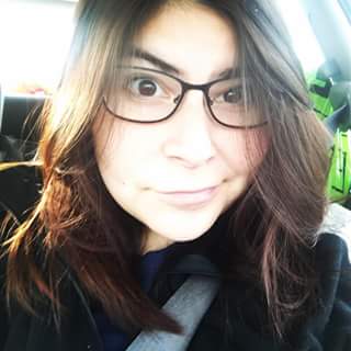 Headshot of a woman with long brown hair, wearing glasses and raising her eyebrows at the camera.