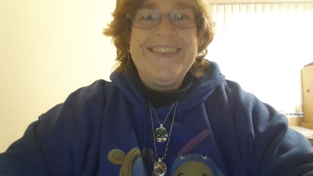 White woman with short blonde hair wearing a blue hoodie, smiling.