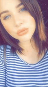 A woman leaning her head to the side and pursing her lips, wearing a white and blue striped shirt