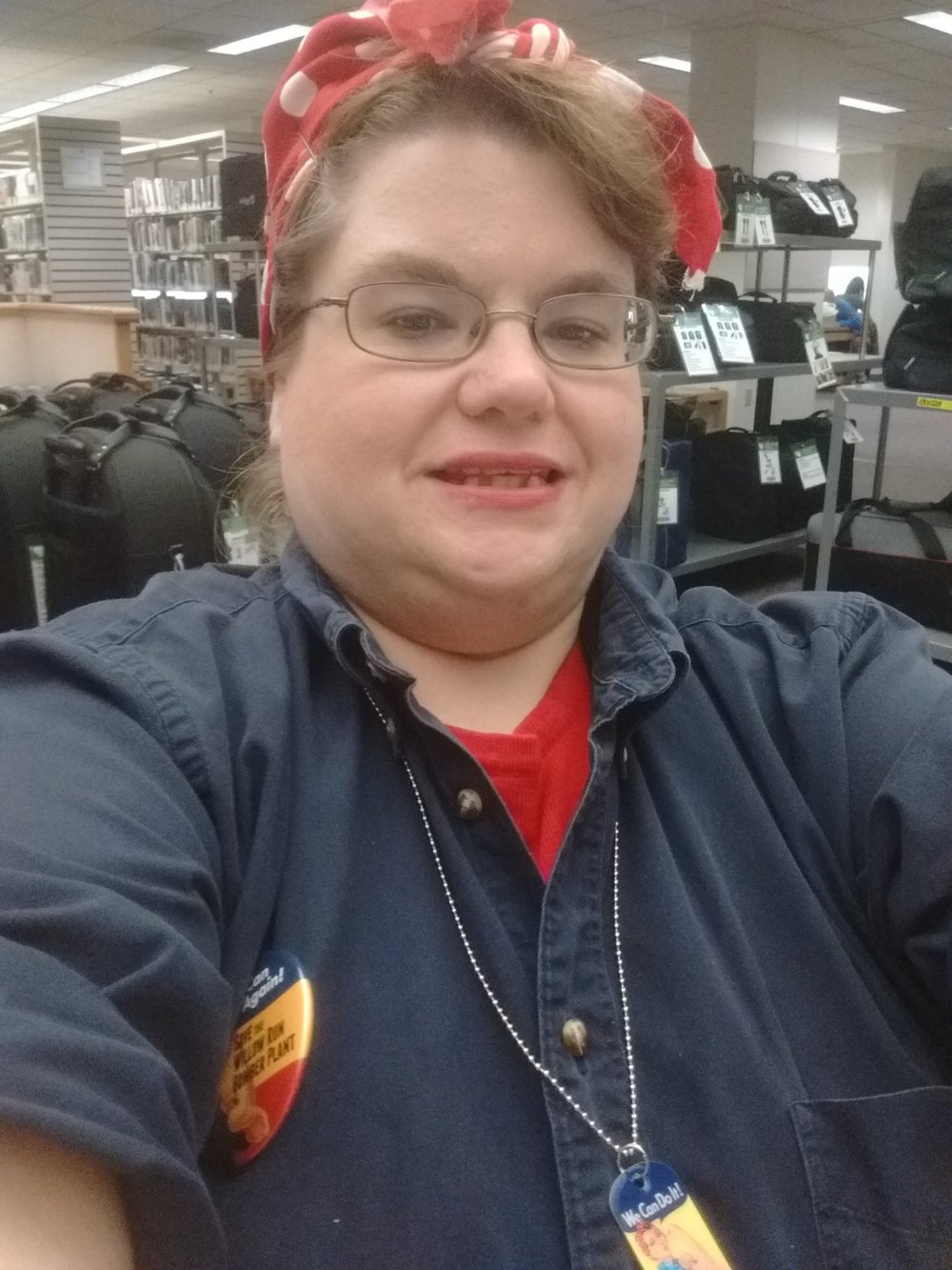 Headshot of a woman wearing a red bandana around her head and a blue collared shirt. She smiles at the camera. 