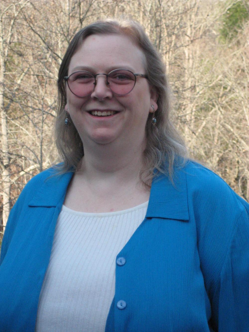 woman-near-woods-with-thin-blonde-hair-and-blue-overshirt-wearing-pink-eyeglasses