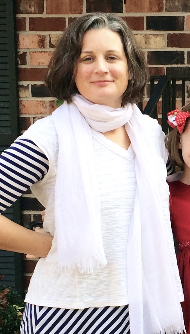 woman-with-short-brown-hair-in-a-white-shirt-and-blue-and-white-shirt-underneath-standing-with-her-right-hand-on-hip
